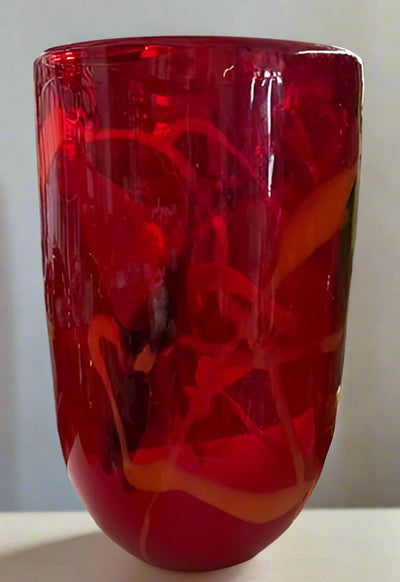 Vibrant red glass vase with other decorative items on a table in a store setting.