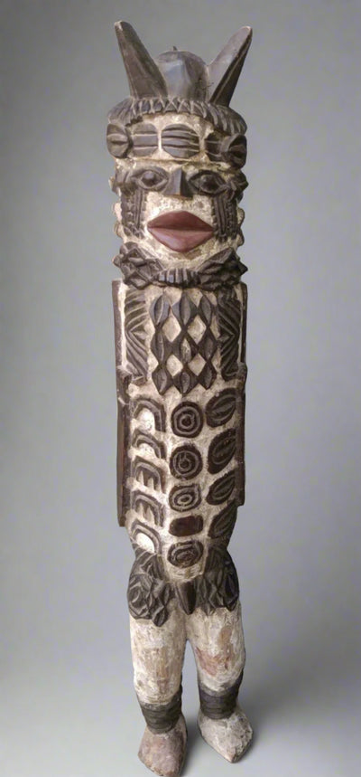 Carved wooden figure with intricate patterns against a stone wall.
